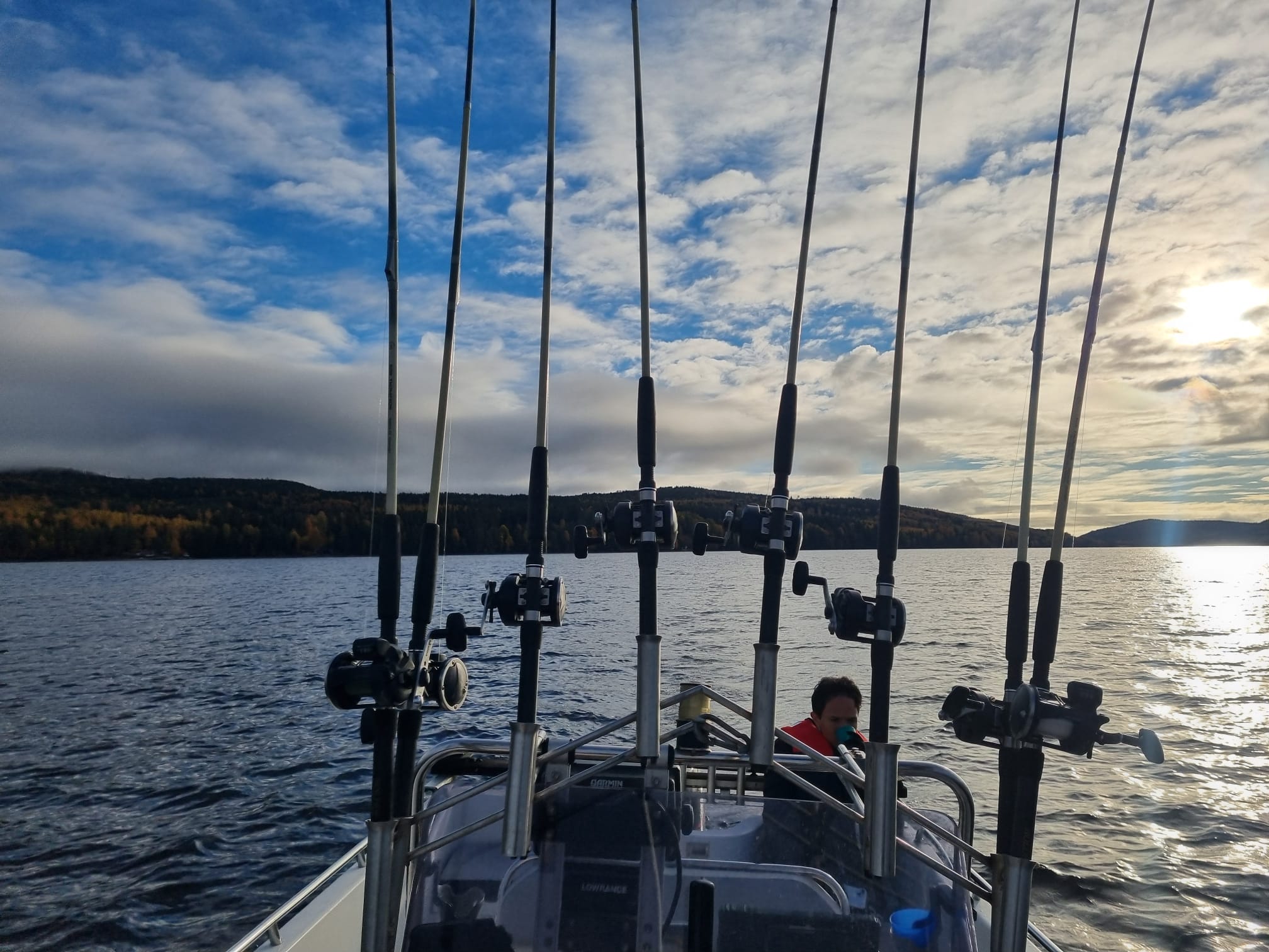 Åtta trollingspön i grind på KingFishings båt i kvällsljus över Dellen, med höstfärgade berg i bakgrunden